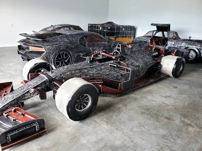 Full-scale F1-inspired metal race car in the fabrication studio beside other full-scale builds