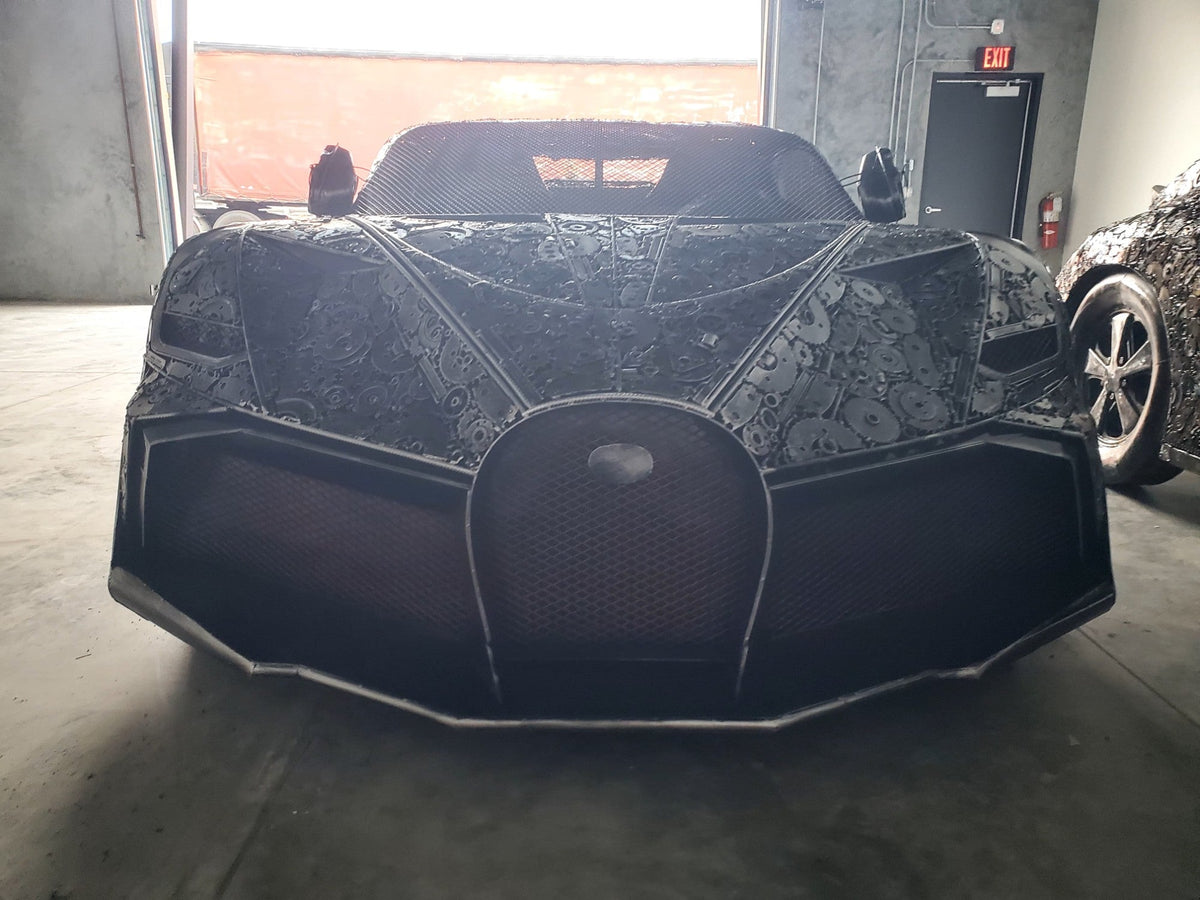Chiron-inspired full-scale hypercar recycled metal sculpture in dramatic warehouse light